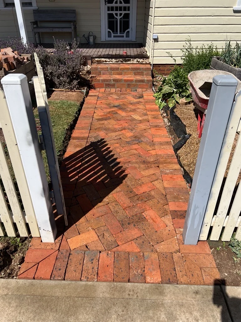 Brick entry path and steps through a white picket gate