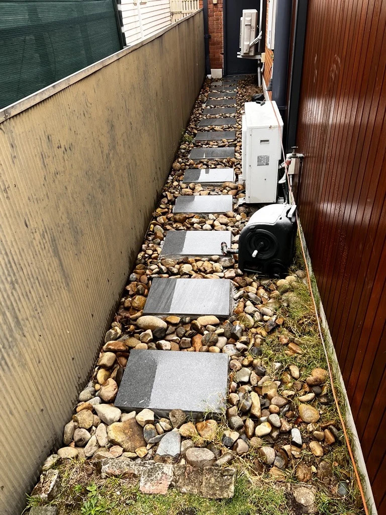 Square stepping stones through a narrow pebble-lined side access